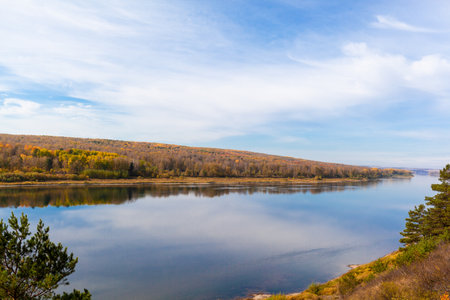 Beautiful, wide autumn river among forests and rocky shore. A calm and quiet place with autumn colors. Reflection of clouds in the water in good weatherの写真素材