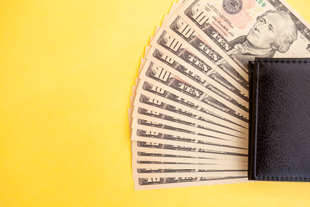 Ten dollar bills banknotes inside a black wallet on yellow background, cash paper currency, payment, earning and savings, money and finance conceptの写真素材