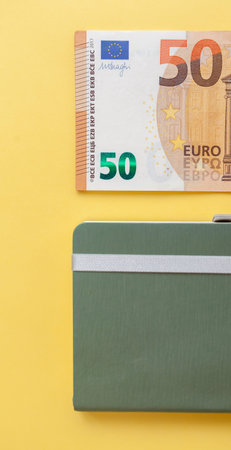 Fifty euro banknotes inside a black wallet on yellow background