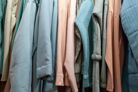 Colorful women's dresses, jackets, trousers and other clothes on hangers in a retail store. The...
