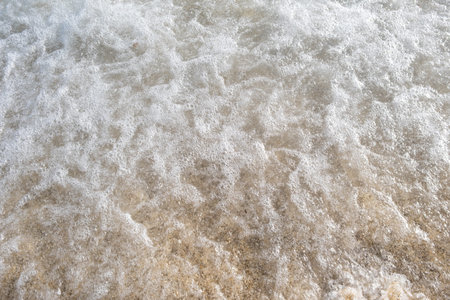 A soft wave runs on a sandy shore on a summer day.