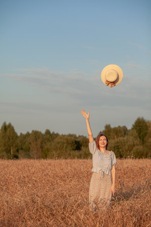 A girl holds a hat in her hand against the background of a wheat fieldの写真素材