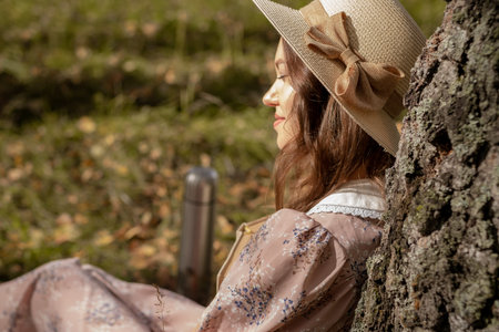 A young beautiful woman in a dress and a round hat reads a book