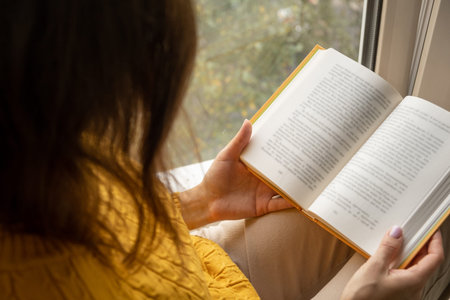 Young beautiful woman near window yellow knitted sweater read book