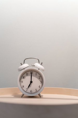 Close-up of a round white alarm clock on a table in the bedroom.