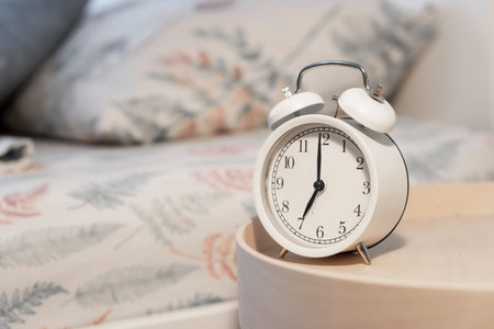 Close-up of a round white alarm clock on a table in the bedroom.