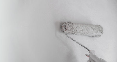 Painting a bare wall with a roller with white paint. Apartment painting