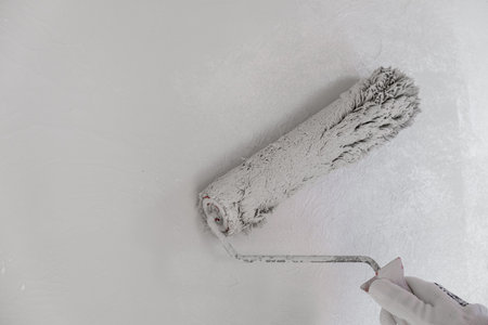 Painting a bare wall with a roller with white paint. Apartment paintingの写真素材