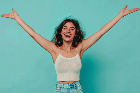 A woman dressed in a white knitwear singlet stands against a turquoise background, her arms outstretched in a gesture of excitement and joy. Her joyful expression and open arms suggest a celebrationの素材