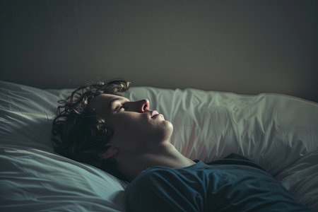 A young man lies in bed, staring blankly at the ceiling. The room is dimly lit, and the background is blurred, creating a sense of emptiness and despair.の素材