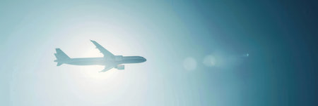 A minimalistic silhouette of an airplane flying through a bright blue sky. The airplane is positioned in front of the sun, creating a radiant glow.の素材