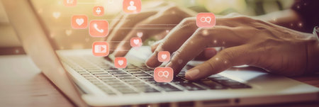 A close-up shot of hands typing on a laptop keyboard, with social media icons hovering around them. This image represents digital engagement and productivity.の素材