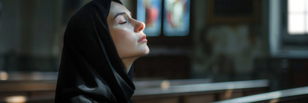 A caucasian nun dressed in a black habit is deep in prayer, eyes closed, in the serene atmosphere of a church.の素材