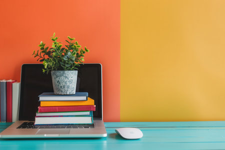 A laptop sits on a stack of colorful textbooks with a small plant, symbolizing modern education.の素材