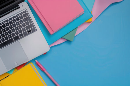 A laptop computer and colorful textbooks arranged on a blue desk, symbolizing contemporary learning methods.の素材