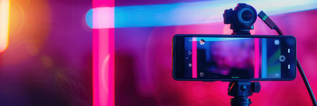 A smartphone on a tripod captures video footage in a studio setting with colorful lighting.の素材