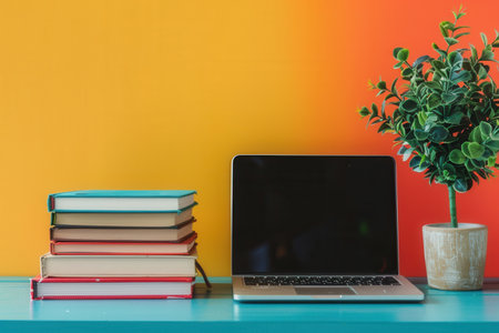 A laptop and a stack of textbooks sit on a colorful desk, representing modern methods of learning.の素材