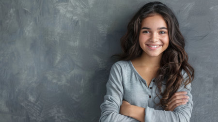 A portrait of a young Hispanic woman with a pleasant smile, standing against a gray wall with her arms crossed. She is looking directly at the camera.の素材