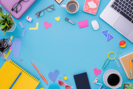 A modern office workspace with colorful supplies and devices on blue background, including laptop, pens, notebook, and other essentials.の素材