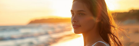 A young woman stands on a beach at sunset, enjoying her summer vacation.の素材
