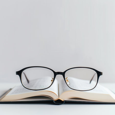 Black eyeglasses rest on an open book against a white background.の素材