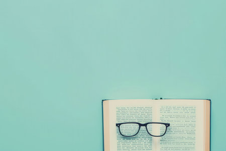 A book lies open on a light blue background, with eyeglasses resting on the open pages.の素材