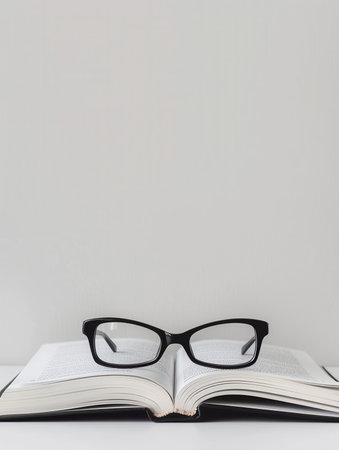 A black-framed pair of eyeglasses rests on top of an open book.の素材