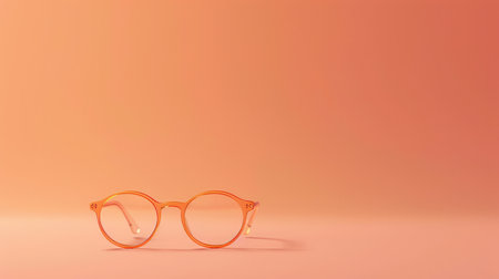 Orange-framed glasses sit on a peach-colored surface.の素材
