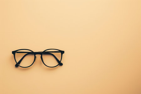 A pair of black framed glasses sit on a peach-colored surface.の素材