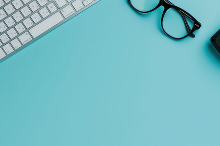A white keyboard and black eyeglasses are placed on a light blue background.の素材