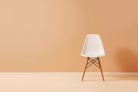 A white chair with wooden legs sits in front of a light peach wall.の素材