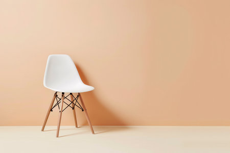 A white plastic chair with wooden legs and black webbing sits in front of a peach wall.の素材
