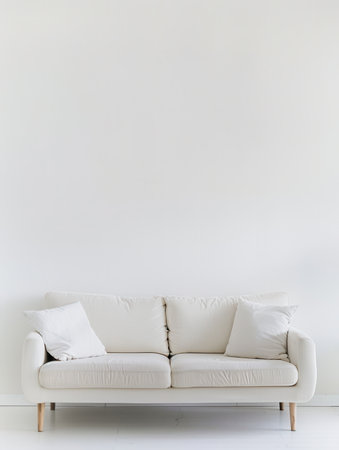 A white sofa sits centered against a blank wall, with two pillows on each end.の素材