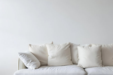 A white sofa with multiple pillows sits against a white wall. The sofa and pillows are all white, creating a clean and minimalist aesthetic.の素材