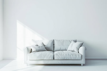 A white couch sits in a room with white walls and minimal furniture. The sun shines through a window, casting a bright light on the couch.の素材