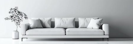 A white sofa with four cushions sits against a plain white wall. A small plant is in a white pot to the left of the sofa.の素材