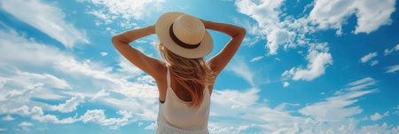 A woman wearing a summer outfit stands on the beach, basking in the warmth of a sunny day, surrounded by a clear blue sky dotted with clouds.の素材