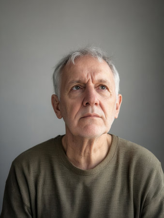 An elderly man with gray hair looks upward, reflecting in a minimalistic indoor space. Natural light softly illuminates his contemplative expression.の素材