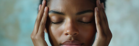 A person sits quietly with closed eyes and hands on their head, visibly expressing feelings of stress and anxiety in a calm indoor setting.の素材