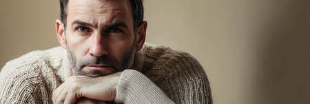 The man reflects deeply, showing seriousness and contemplation in a cozy, softly lit indoor environment.の素材