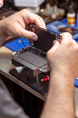 A technician carefully disassembles a smartphone to replace its battery in a well-equipped repair shop.の写真素材