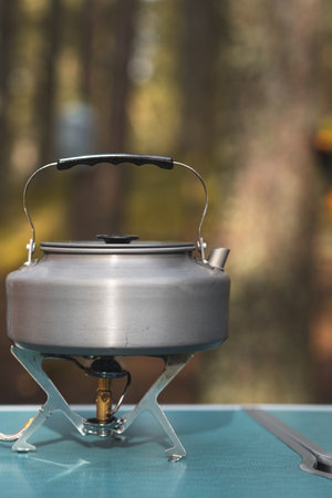 A silver kettle heats water on a portable stove, surrounded by peaceful woods in the warm glow of late afternoon light.の写真素材