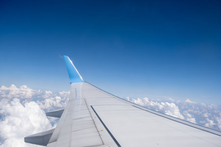 View from the airplane window of the wing and winglet soaring through a clear blue sky with clouds belowの写真素材