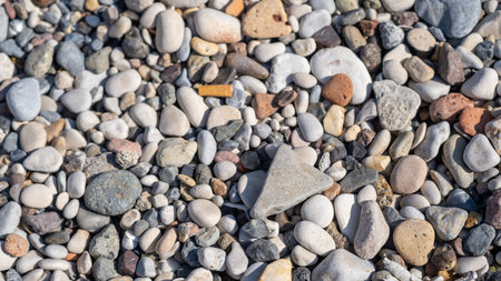 A diverse collection of small stones and pebbles lies on the beach, glistening in bright sunlight on...