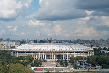 Luzhniki Park features the grand stadium set amid lush greenery and panoramic urban skyline under a dramatic cloud-filled sky.の写真素材