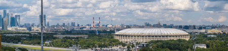 The iconic Luzhniki Stadium is nestled within Luzhniki Park, with the modern Moscow City skyline rising in the background under blue skies.の写真素材