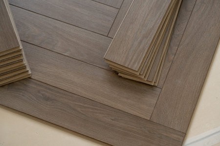 Worker installing laminate flooring in a residential apartment. Tools, planks, and underlay are...