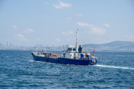 A blue cargo boat travels across calm waters with the Istanbul skyline visible in the background on...