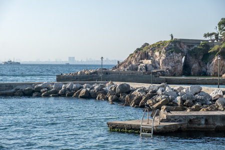 The sun sets over a peaceful coastal area, highlighting rocks and calm waters near a historic fort by the sea.の写真素材