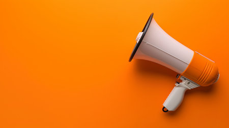 The bright orange megaphone leans on a matching surface, highlighting its purpose for making announcements and drawing attention.の素材